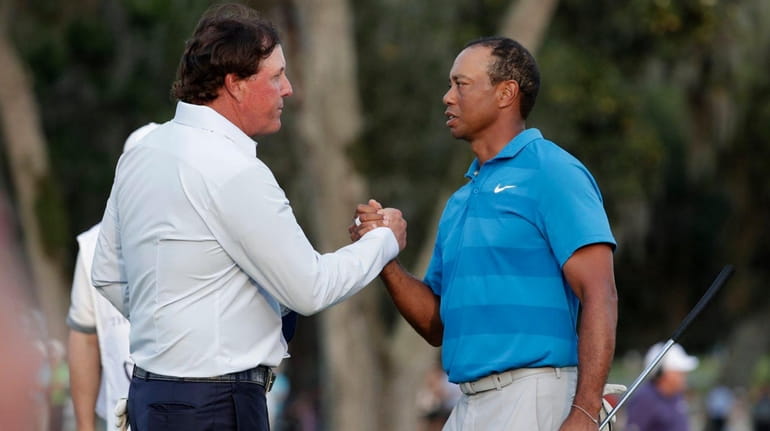 Phil Mickelson, left, and Tiger Woods shake hands after the...