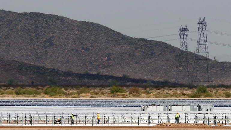 Workers continue to build rows of solar panels at a...