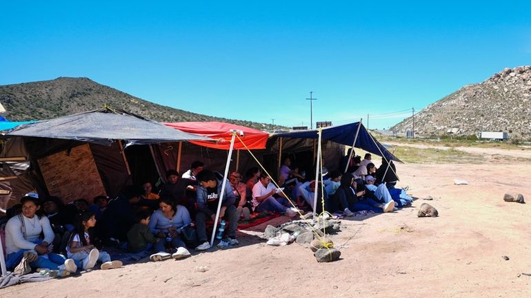 A group of people wait to be processed after crossing...