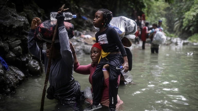 Haitian migrants wade through water as they cross the Darien...