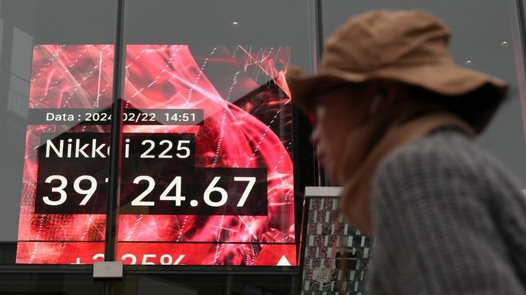 A person walks in front of an electronic stock board...