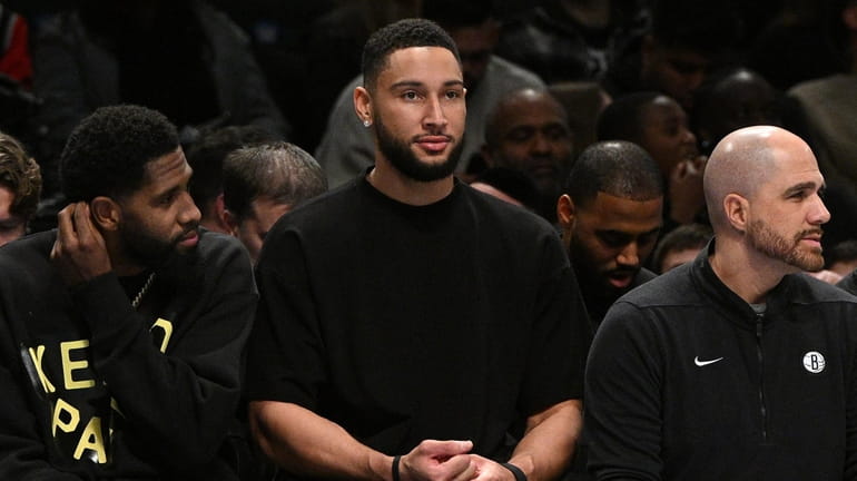 Nets guard Ben Simmons, center, in street clothes, looks on...