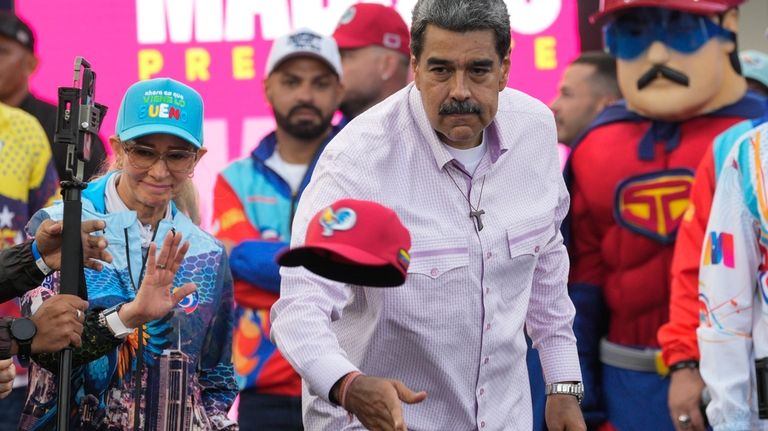 Venezuelan President Nicolas Maduro throws a cap to supporters during...