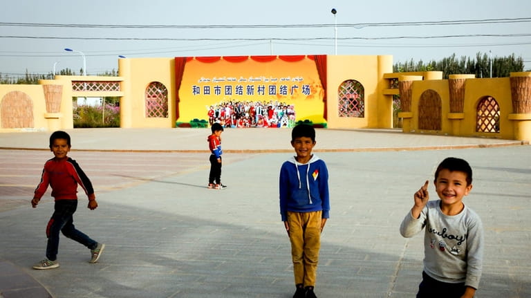 Uyghur children play at a square where a propaganda poster...