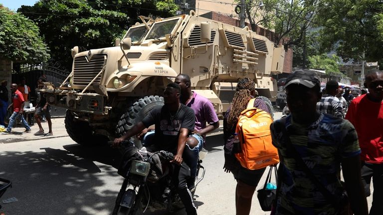 Pedestrians walk past an armored police vehicle carrying Kenyan police...