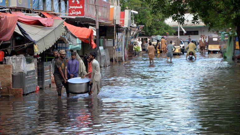 People wade through a flooded road caused by heavy monsoon...