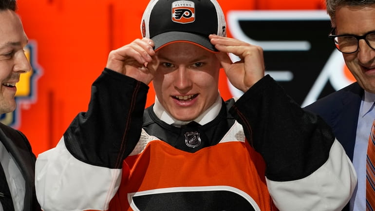 Matvei Michkov, center, adjusts his Philadelphia Flyers cap after being...