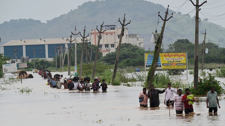 People, many carrying their belongings, wade through a flooded road...