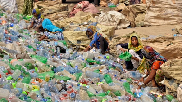 Pakistani laborers, mostly women, sort through empty bottles at a...