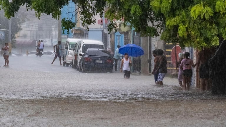 People walk through a street flooded by the rains of...