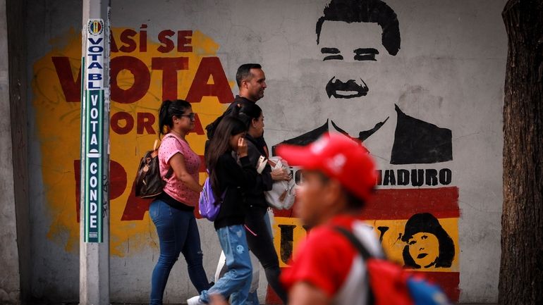 Pedestrians walk past a campaign mural featuring President Nicolas Maduro,...