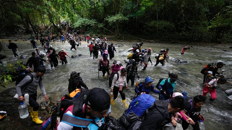 Migrants cross a river during their journey through the Darien...