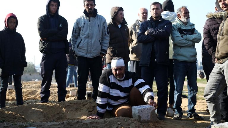 Palestinians stand around the grave of a relative killed in...