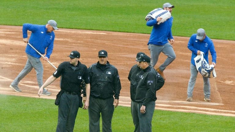 The umpires talk as the grounds crew work on the...