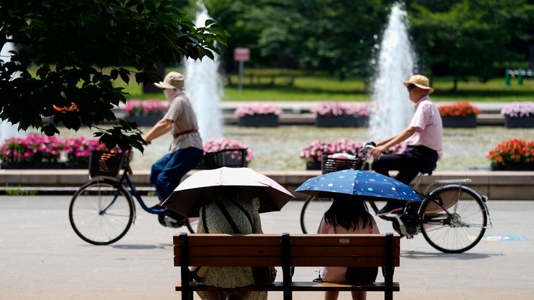 People holding parasols sit on the bench under an intense...