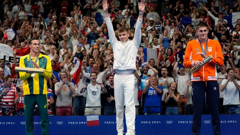 Gold medalist Leon Marchand, center, of France, waves as he...