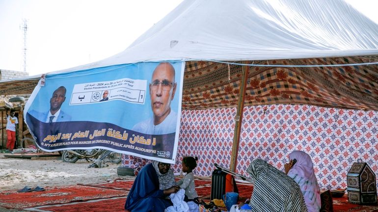 Women sit behind an electoral banner for Mauritanian president Mohamed...