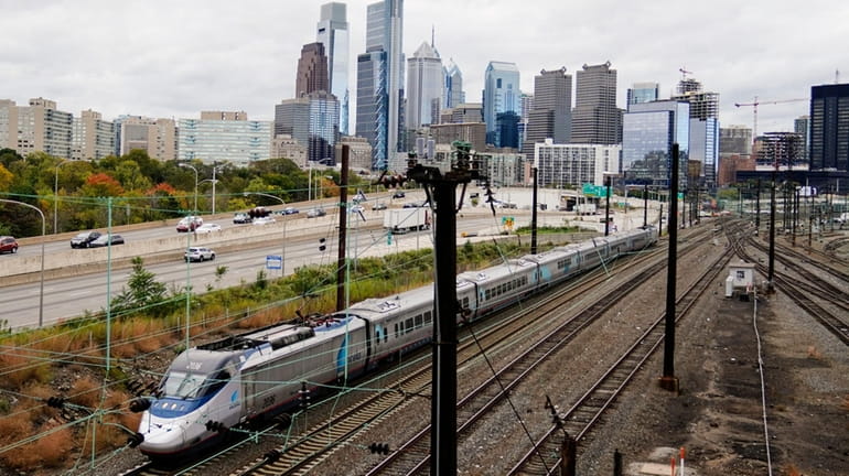 An Amtrak train departs 30th Street Station traveling parallel to motor...