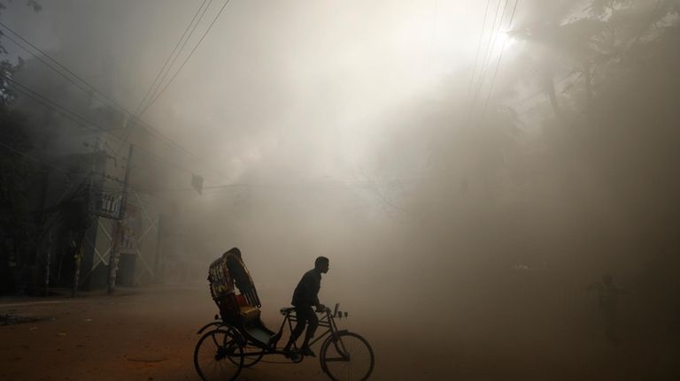 A rickshaw puller rides in the smoke caused by a...