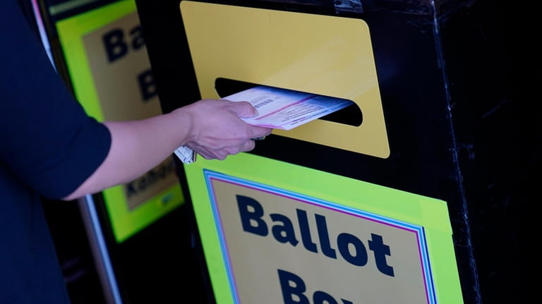 A person places mail-in ballots at a mail-in ballot drop...
