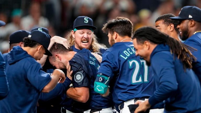 Seattle Mariners' Cal Raleigh is mobbed by teammates, including relief...