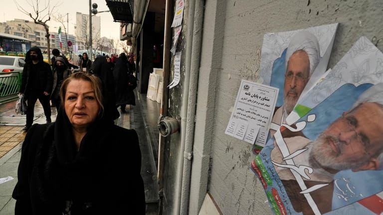 A woman walks past electoral posters of Ayatollah Alireza Arafi,...