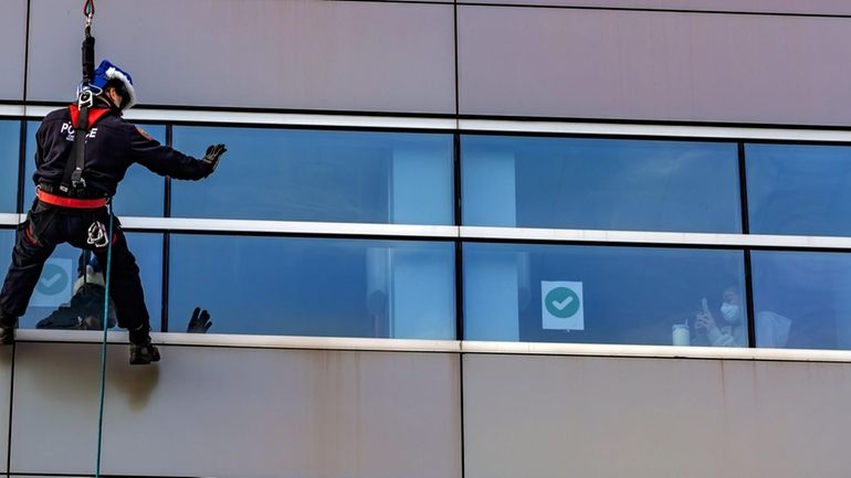 A member of the Nassau police Emergency Services Unit rappelling team greets...