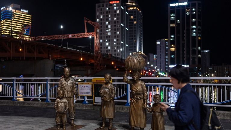 A woman walks past bronze sculptures portraying Korean War refugees...