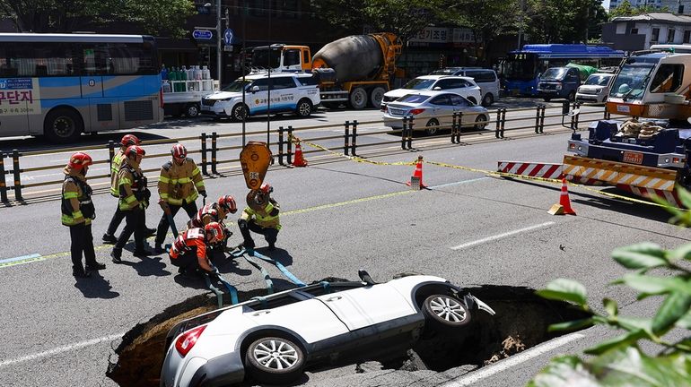 South Korean firefighters prepare to lift a vehicle that fell...