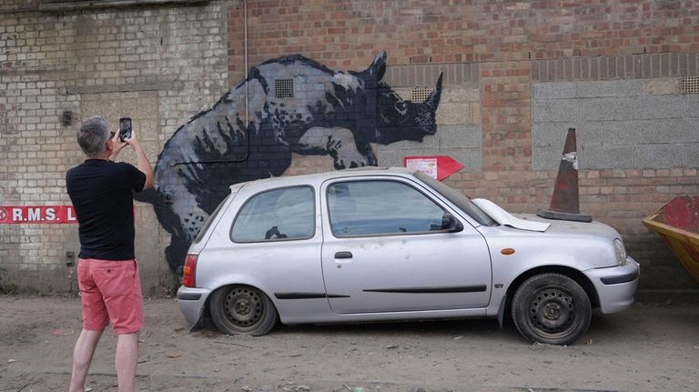 A man photographs a new artwork unveiled by Banksy, depicting...