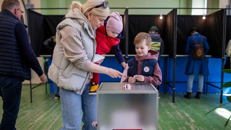 A woman with children casts a ballot at a polling...