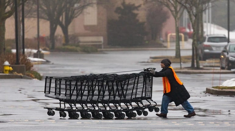 An employee pushes shopping carts as light rain falls outside...
