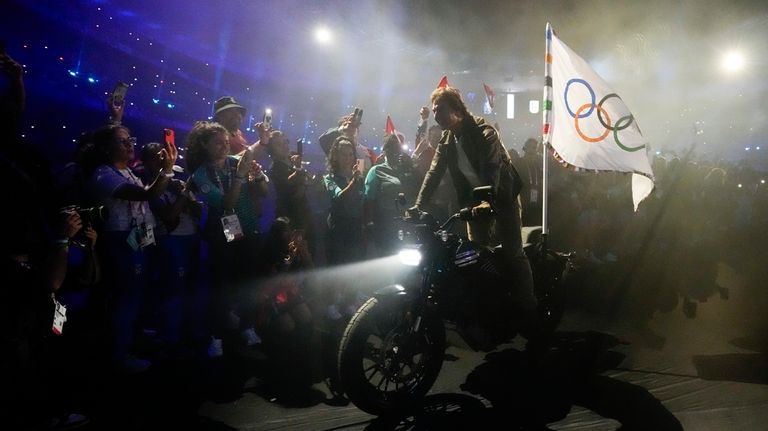 Tom Cruise rides a motorbike with the Olympic flag attached...