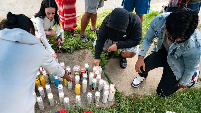 People light candles on the sidewalk during a vigil for...