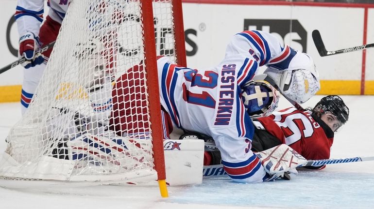 The Devils' Jack Hughes, right, tries to get up after...