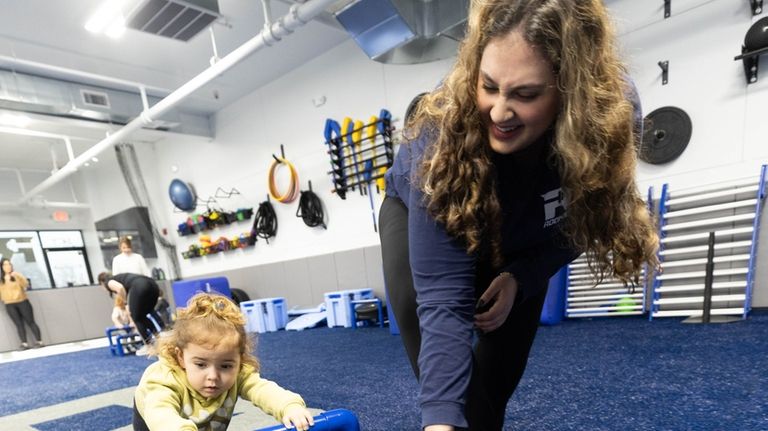 Two-year-old Sadie Loesch pushes a sled with the help of...