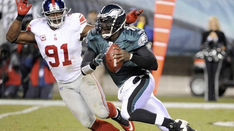 Philadelphia Eagles quarterback Michael Vick scrambles past New York Giants...