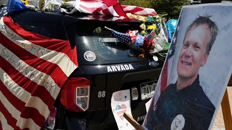 Flowers, flags and notes cover a patrol car outside Arvada...