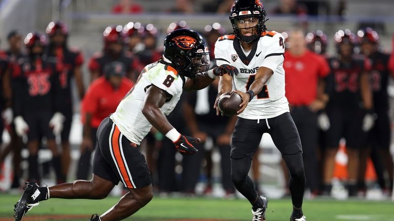 Oregon State quarterback Gevani McCoy, right, hands off the ball...