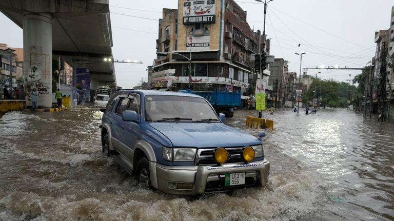 Cars drive through a flooded road caused by heavy monsoon...