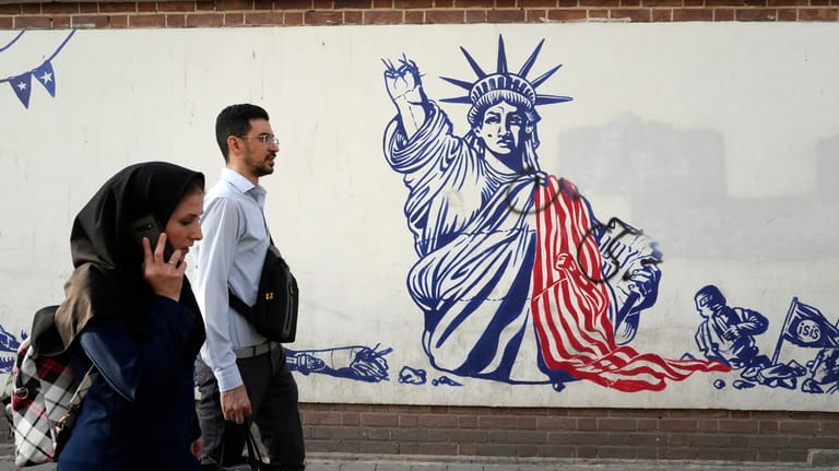 People walk past a state-organized, anti-U.S. mural painted on the...