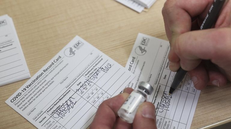 A health care worker fills out a COVID-19 Vaccination Record...