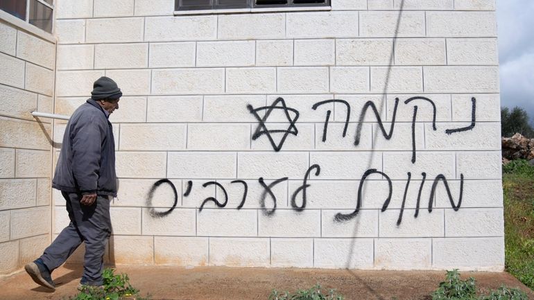 A man looks at graffiti that reads, in Hebrew, "revenge,...