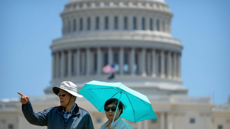Visitors wear sun hats, sunglasses, and carry an umbrella to...