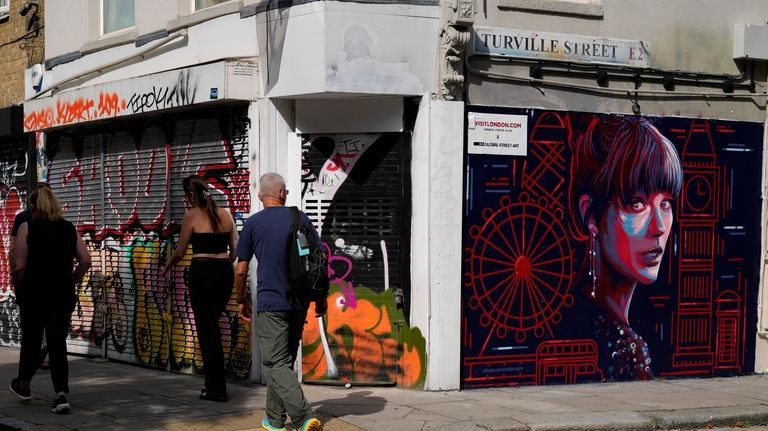 Pedestrians walk past a new mural portrait of Taylor Swift...