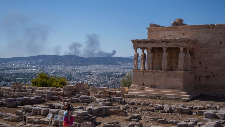 A woman poses for a photo in front Caryatid statues...