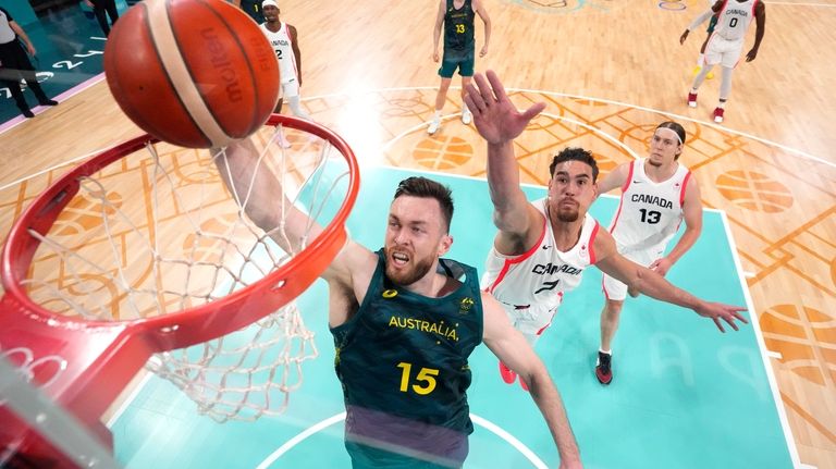 Australia's Nick Kay, left, dunks as Canada's Dwight Powell, center,...