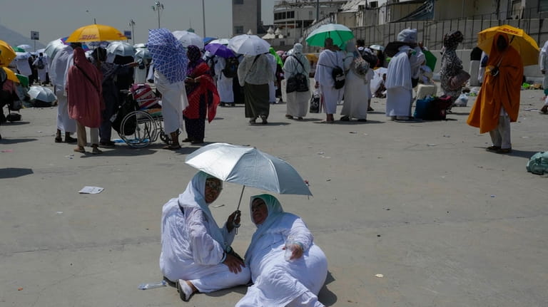 Two muslim pilgrim women share umbrella to protect themself from...