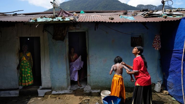 Muthuthewarkittan Manohari, a tea plantation worker, right, bathes her younger...