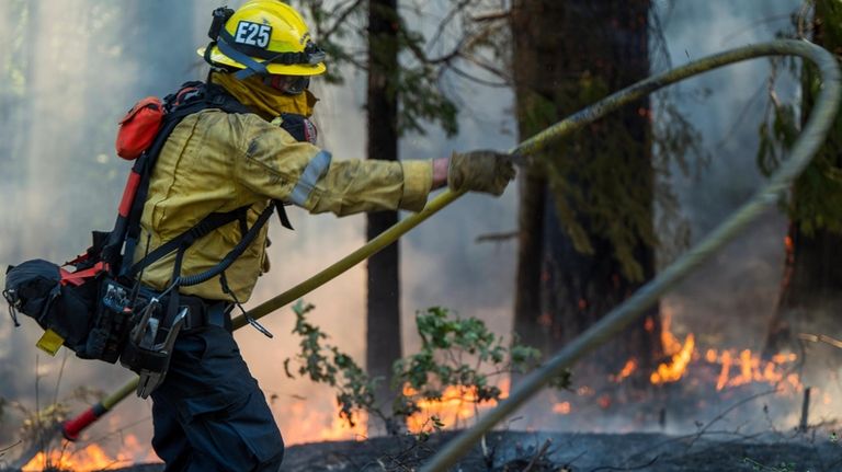 A firefighter lays out a hose line while fighting the...